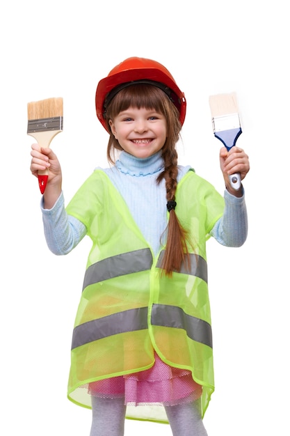 Menina pré-escolar sorridente com capacete e colete de construção com pincel no fundo branco isolado