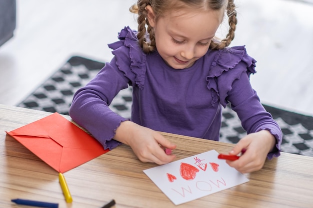 Menina preparando um cartão para a mãe com coração vermelho e letras da mãe como presente para o dia das mães