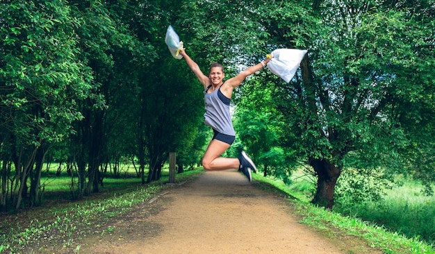 Menina pulando com sacos de lixo depois de plogging