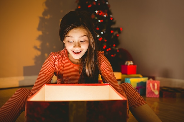 Menina que abre um presente brilhante de Natal