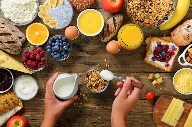 Menina que cozinha o café da manhã - granola com iogurte, frutos, bagas, leite, iogurte, suco, queijo. Comer limpo, dieta, desintoxicação, conceito de comida vegetariana