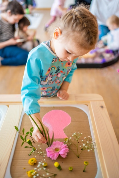 Menina que joga com o jogo sensorial que faz o desenvolvimento sensorial do herbário e experimenta ac temático