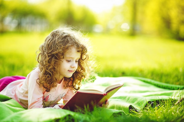 Menina que lê um parque do livro na primavera, tonificando a foto.