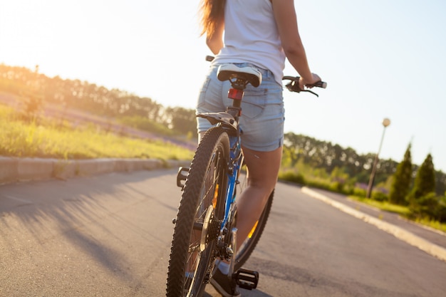 Menina que monta uma bicicleta com calças de brim