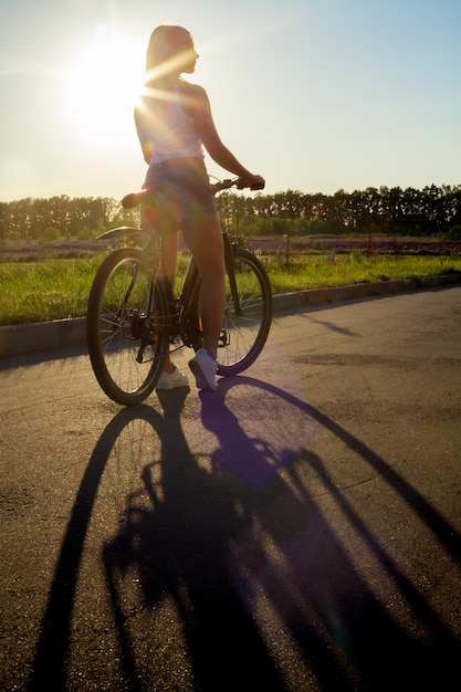 Menina que monta uma bicicleta no por do sol