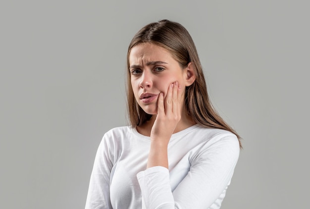 Menina que sofre de dor de dente, cárie ou sensibilidade Dor de dente Mulher com infecção de dente Mulher que sofre de dor de dente contra fundo cinza Jovem mulher que sofre de dor de dente