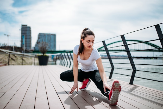 Menina que treina no cais que estica os pés e que faz exercícios.