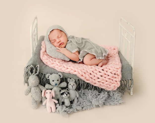 Menina recém-nascida dormindo em uma pequena cama decorada com brinquedos de malha. Adorável criança infantil cochilando durante a sessão de fotos do estúdio