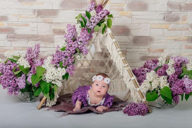 Menina recém-nascida em uma grinalda branca perto de flores lilás primeira sessão de fotos do bebê filhinha