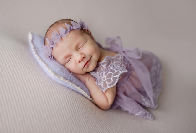 Menina recém-nascida em vestido de renda dorme e sorri em seu sonho em tons de lila foto