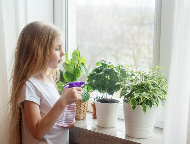 Menina regando plantas domésticas em sua casa