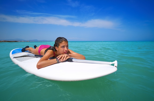 Menina relaxada deitada na prancha de surf paddle