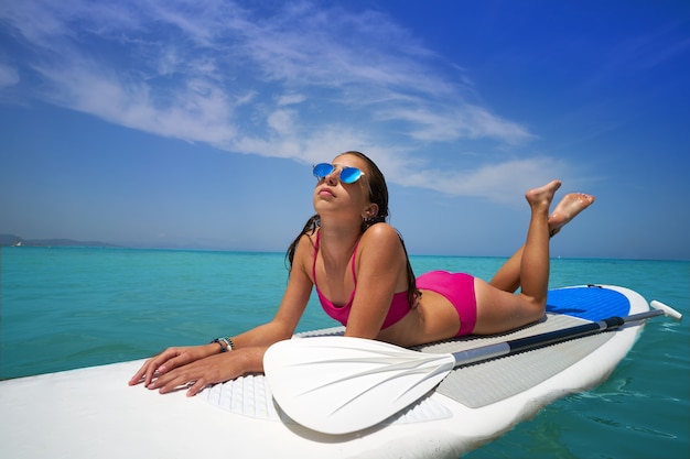 Menina relaxada deitada na prancha de surf paddle