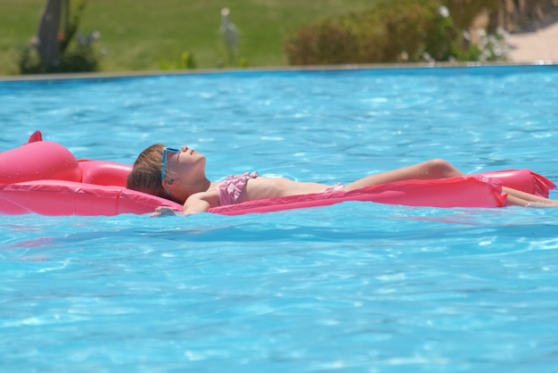 Menina relaxando no sol de verão nadando em um colchão de ar inflável na piscina durante férias tropicais conceito de atividades de verão