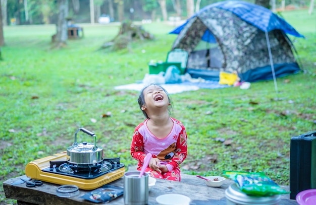 Menina rindo enquanto está sentada à mesa durante o acampamento na floresta