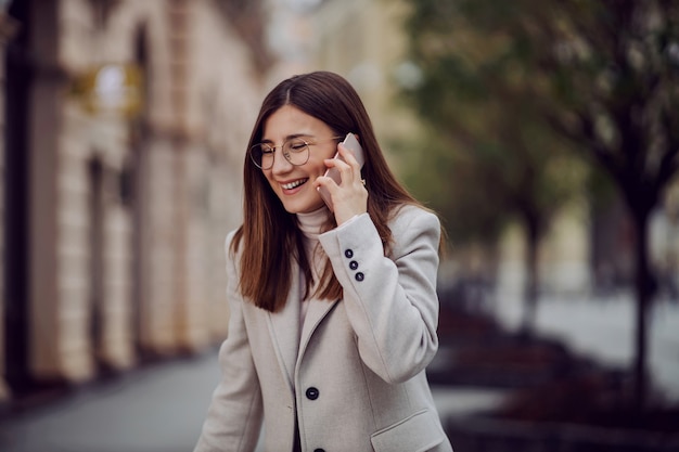 Menina rindo na rua e falando ao telefone. Geração milenar.