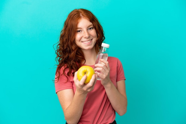 Foto menina ruiva adolescente isolada em fundo azul com uma maçã e uma garrafa de água