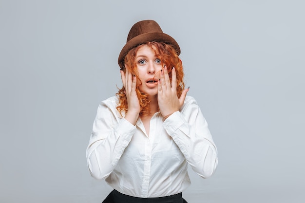 Menina ruiva com chapéu marrom e camisa branca surpresa