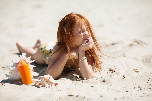 menina ruiva deitada na areia tomando banho de sol