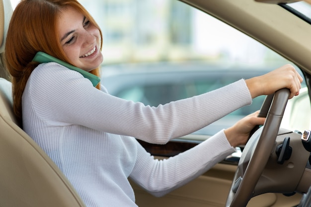 Foto menina ruiva feliz falando em seu telefone celular ao volante, dirigindo um carro.