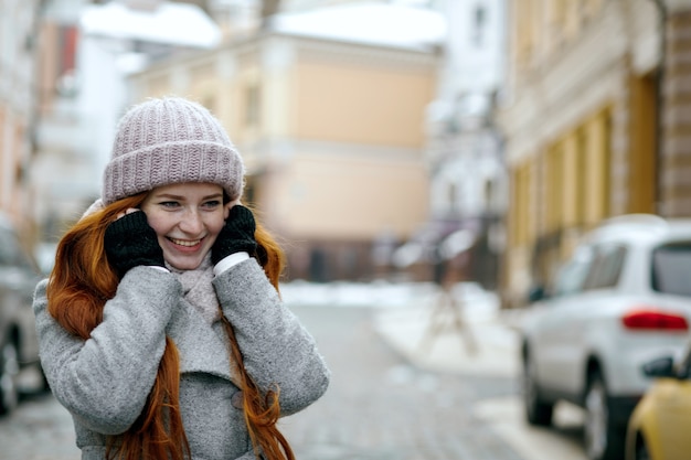 Foto menina ruiva sorridente, vestindo roupas quentes de inverno, andando pela rua. espaço para texto