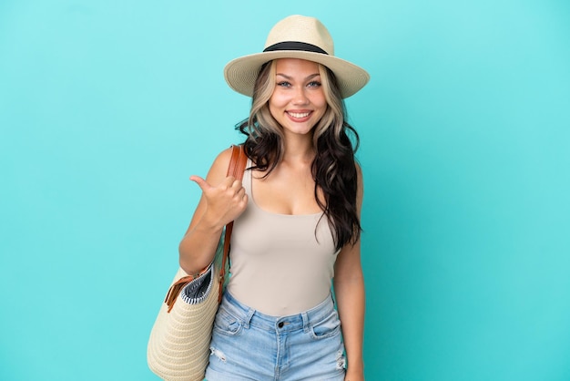 Foto menina russa adolescente com esmalte e bolsa de praia isolada em um fundo azul apontando para o lado para apresentar um produto