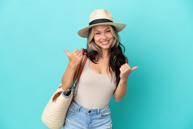 Menina russa adolescente com pamel e bolsa de praia isolada em fundo azul com polegares para cima gesto e sorrindo