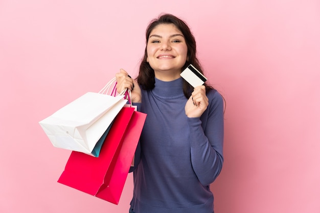 Menina russa adolescente isolada na parede rosa segurando sacolas de compras e um cartão de crédito