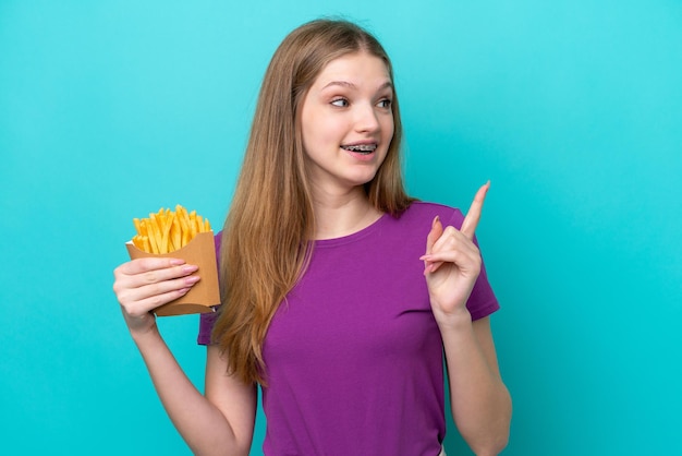 Menina russa adolescente pegando batatas fritas isoladas em fundo azul com a intenção de perceber a solução enquanto levanta um dedo