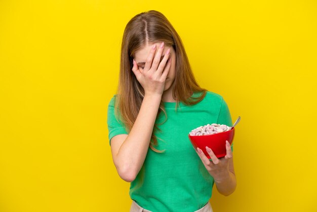 Menina russa adolescente segurando tigela de cereais isolada em fundo amarelo com expressão cansada e doente