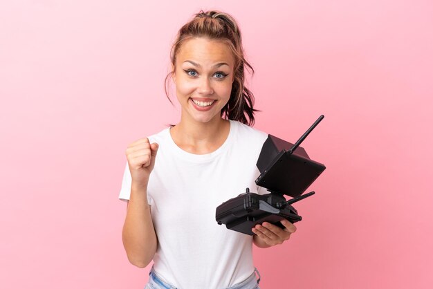 Menina russa adolescente segurando um controle remoto de drone isolado em fundo rosa comemorando uma vitória na posição de vencedor