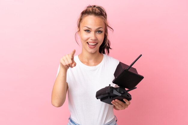 Menina russa adolescente segurando um controle remoto de drone isolado em fundo rosa surpreso e apontando para a frente