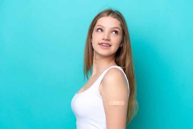 Menina russa adolescente usando um band-aids isolado em fundo azul olhando para cima enquanto sorria