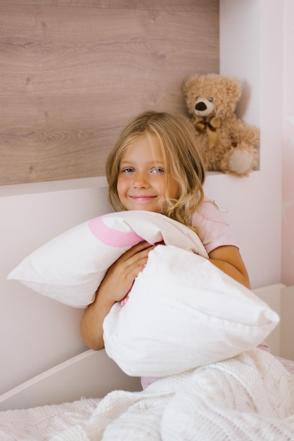 Menina satisfeita feliz sentada na cama abraçando um travesseiro