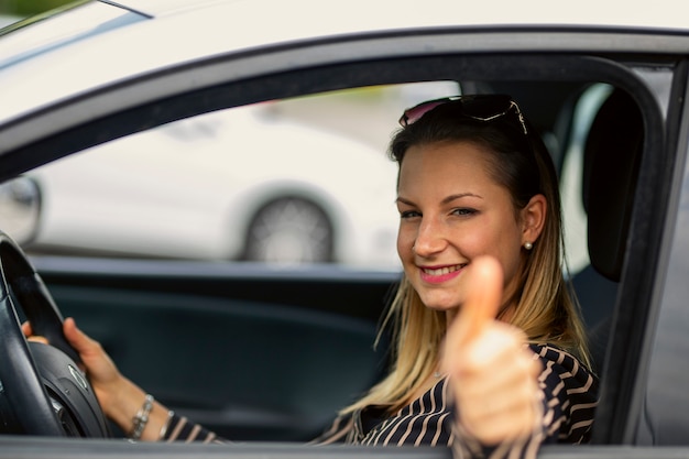 Menina satisfeita, gesticulando polegares para cima sentado dentro de um carro