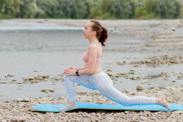 Menina saudável, relaxando enquanto medita e faz exercícios de ioga na bela natureza na margem do rio.