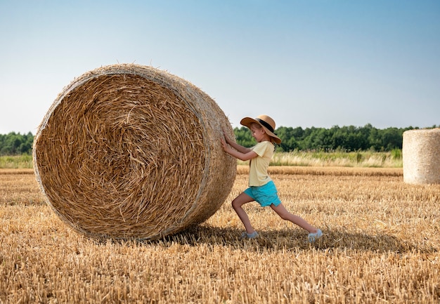 Menina se divertindo em um campo de trigo em um dia de verão. Criança brincando no campo de fardo de feno durante a época da colheita.