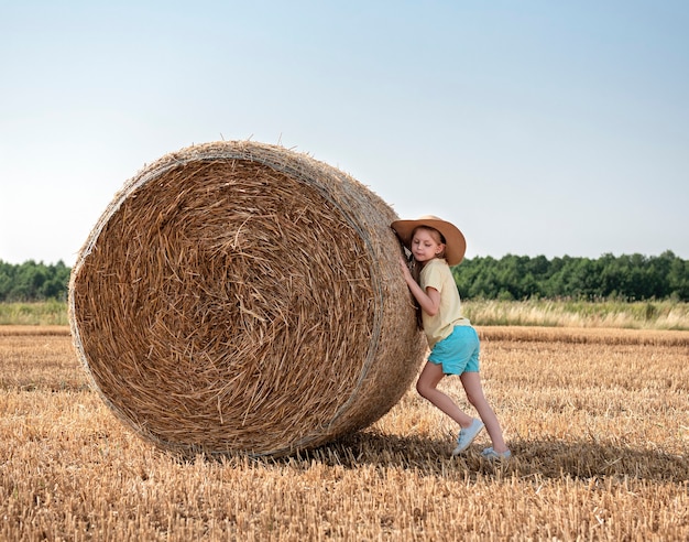 Menina se divertindo em um campo de trigo em um dia de verão. Criança brincando no campo de fardos de feno durante a época da colheita.