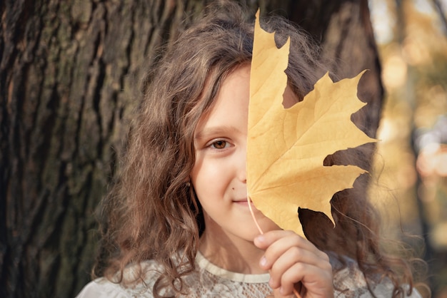 Menina se escondendo atrás da metade de uma folha de outono