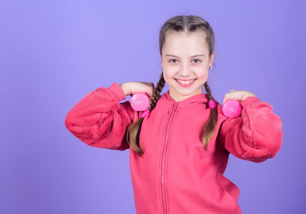 Menina se exercitando com halteres Criança segura fundo violeta de halteres para iniciantes Exercícios com halteres Esporte para adolescentes Exercícios fáceis com halteres Para um corpo mais saudável Conceito de reabilitação