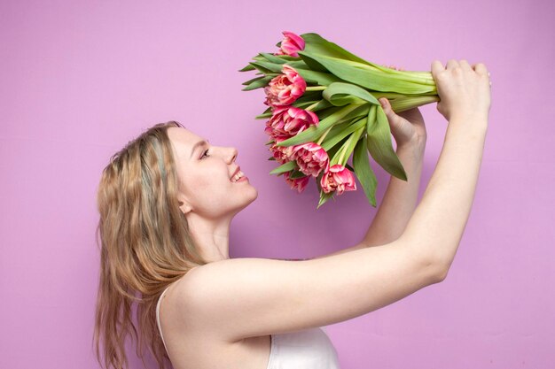 Menina segura e cheira um buquê de flores em um fundo rosa uma linda mulher com tulipas