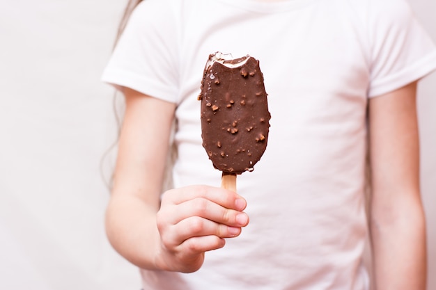 Foto menina segura na mão um picolé mordido em cobertura de chocolate com nozes