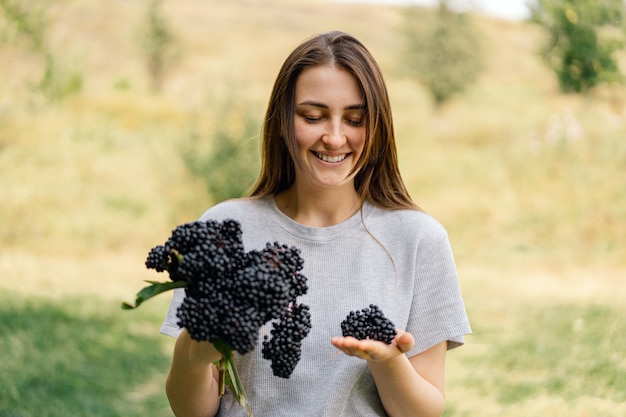 Menina segura nas mãos cachos de fruta preta sabugueiro sambucus nigra preto sabugueiro europeu preto ...