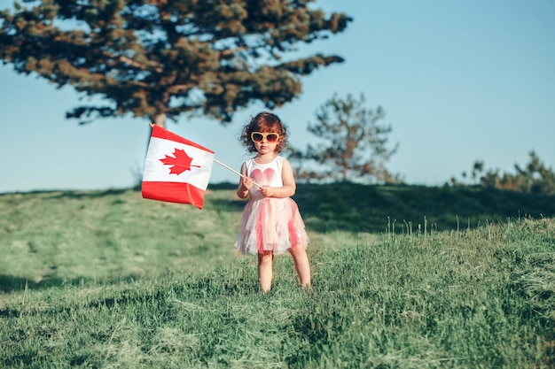 Menina segurando a bandeira canadense enquanto está de pé na grama contra o céu