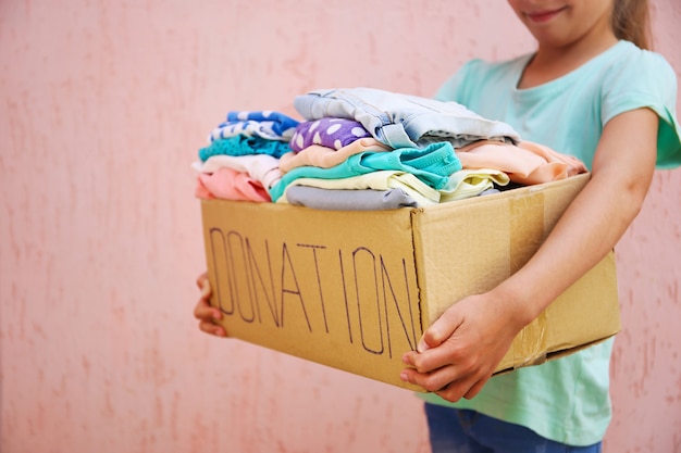 Menina, segurando a caixa de doação com roupas de verão