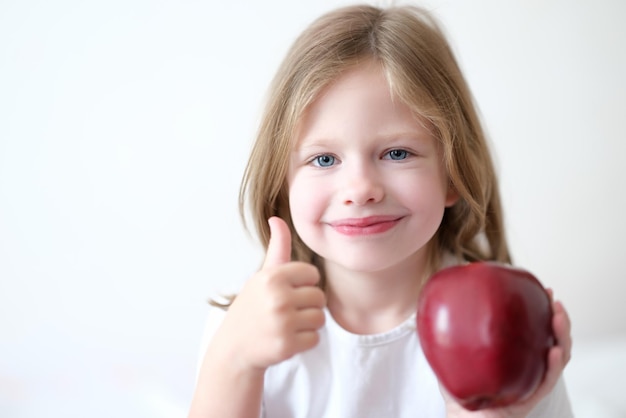 Menina segurando a maçã vermelha nas mãos e mostrando os polegares