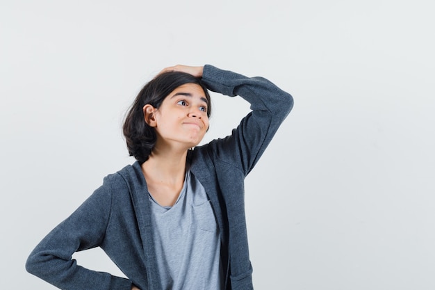 Menina segurando a mão na cabeça em t-shirt, jaqueta e parecendo um sonho, vista frontal.