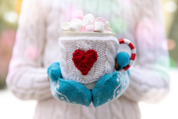 Menina segurando a xícara de chocolate quente nas mãos ao ar livre no inverno. feminino camisola e luvas com enfeite de natal. conceito de férias de natal