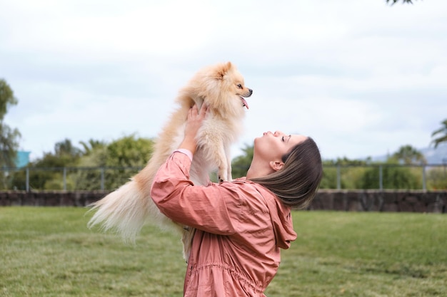Menina segurando e olhando para seu cachorro da Pomerânia com os braços enquanto manda um beijo no ar