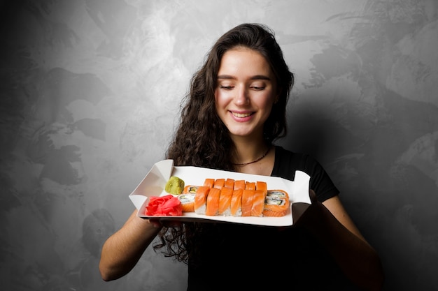 Menina segurando filadélfia rola em uma caixa de papel em fundo cinza. sushi, entrega de comida.